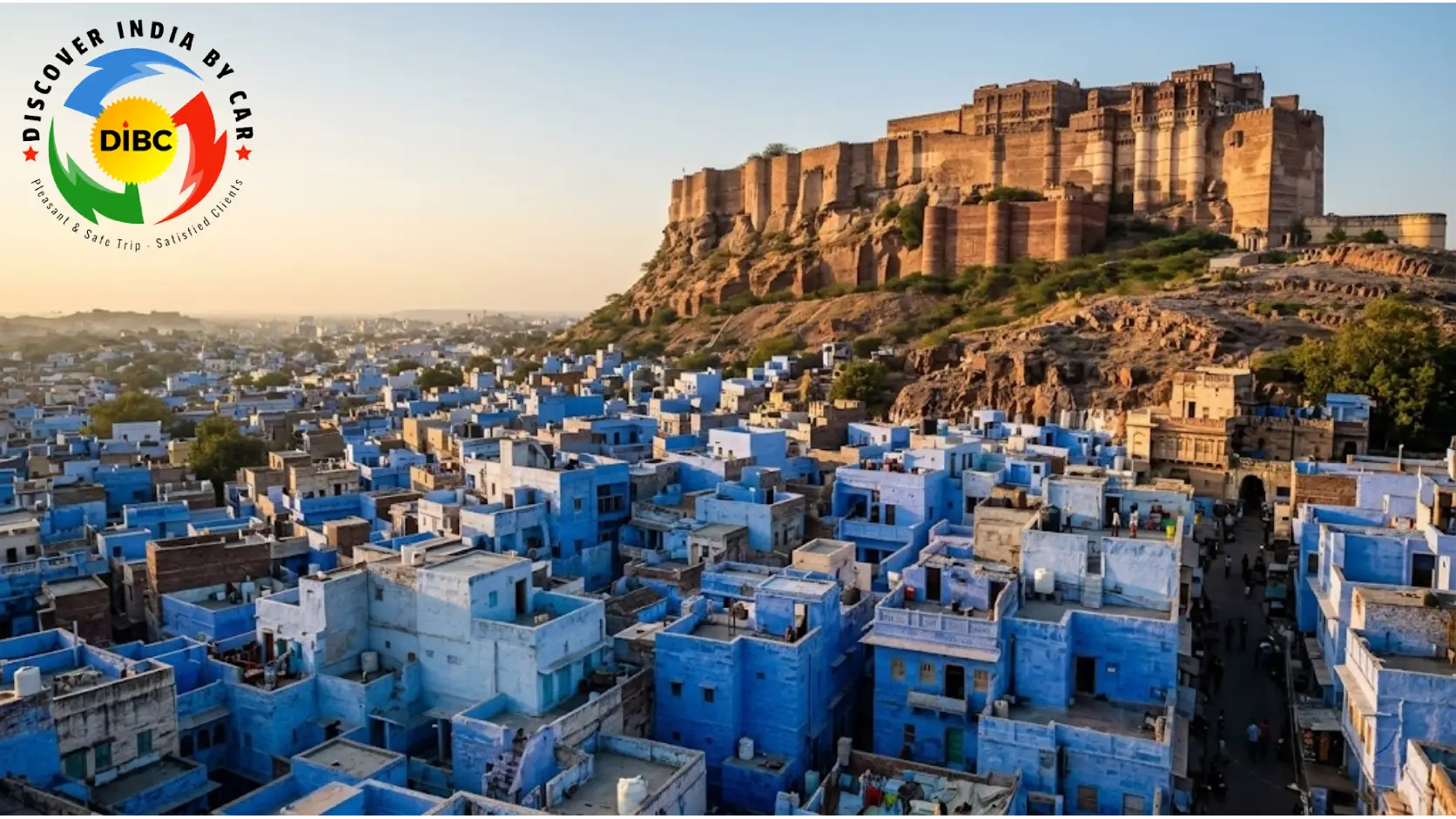 Panoramic wide-angle view of the blue houses in Jodhpur old town nesting below the massive sandstone cliffs of Mehrangarh Fort during evening golden hour